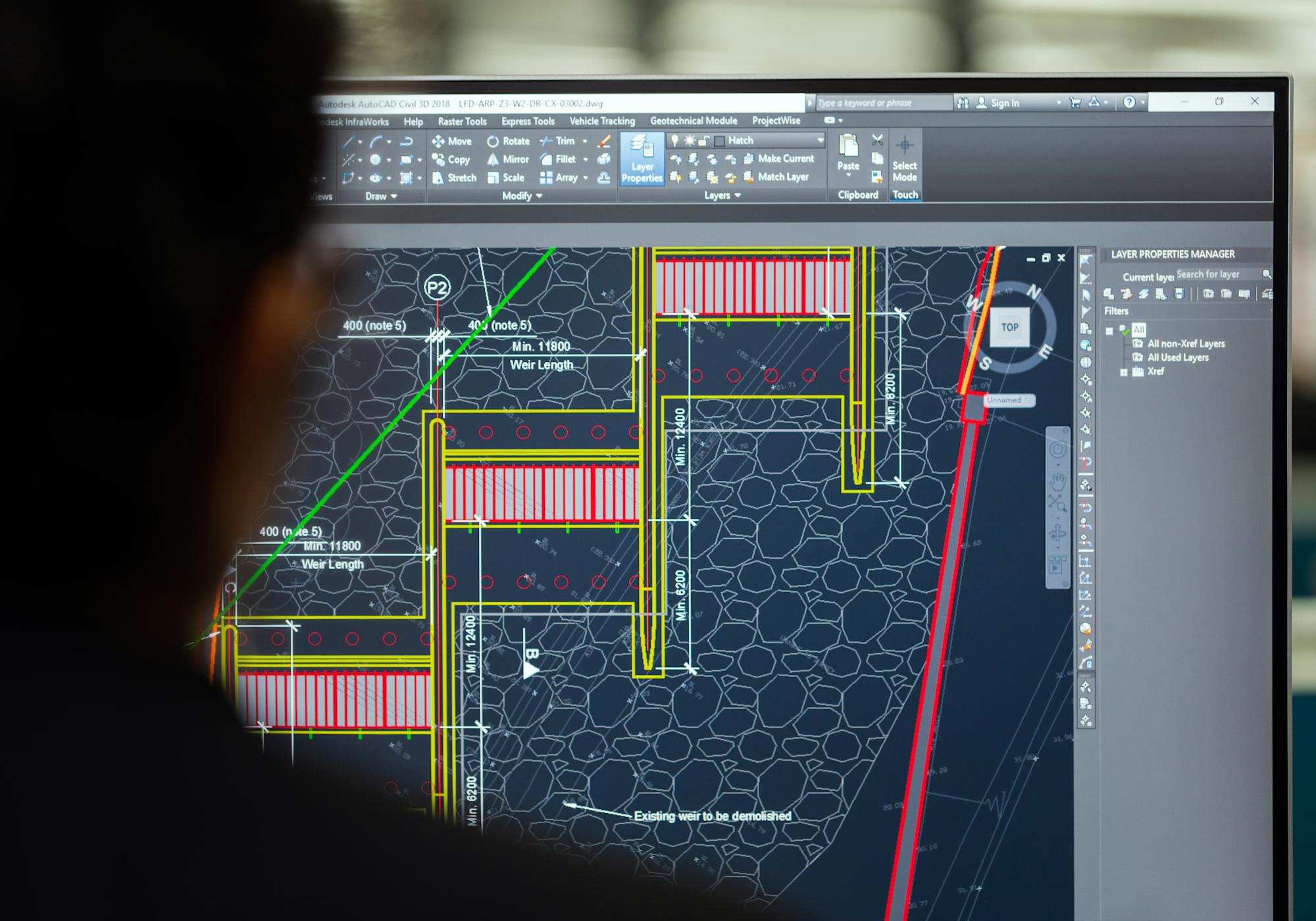 Civil engineer reviewing a weir design in AutoCAD Civil 3D, with reinforcement detail and dimensions visible on the screen